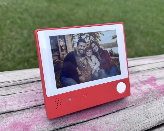 A production Wherezit unit outdoors on a wooden table, its screen showing an example photo.