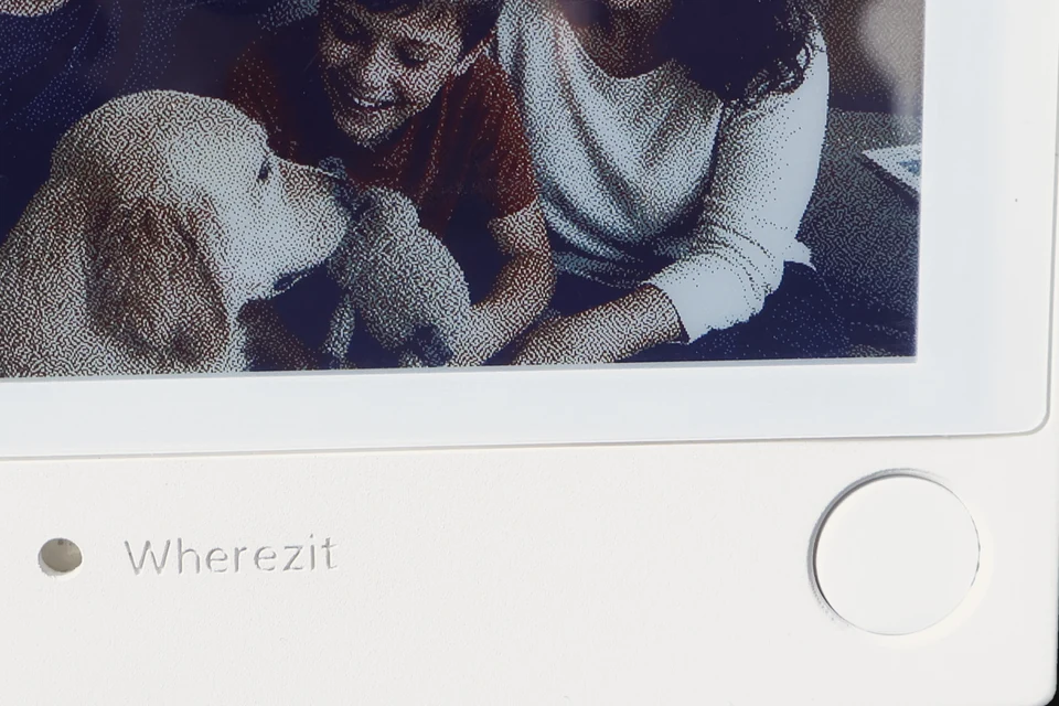 Close-up of the press-and-hold button on a white Wherezit e-paper photo frame.